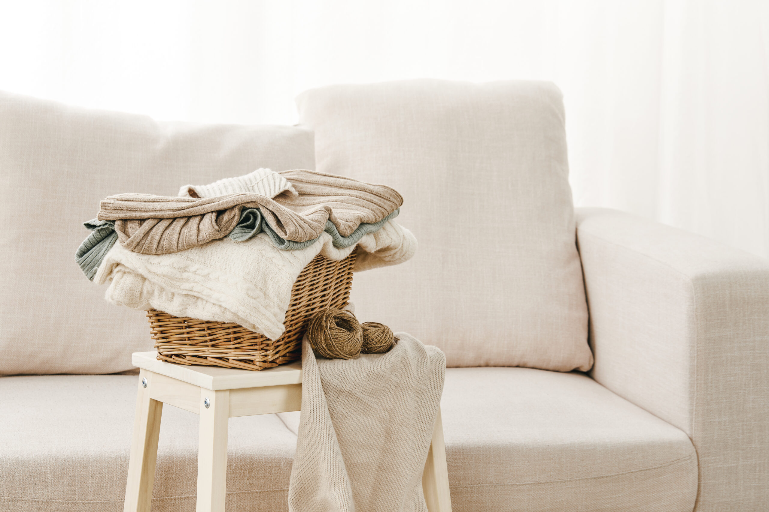 Closeup of a gray sofa with a basket of folded clothes on a small table near it